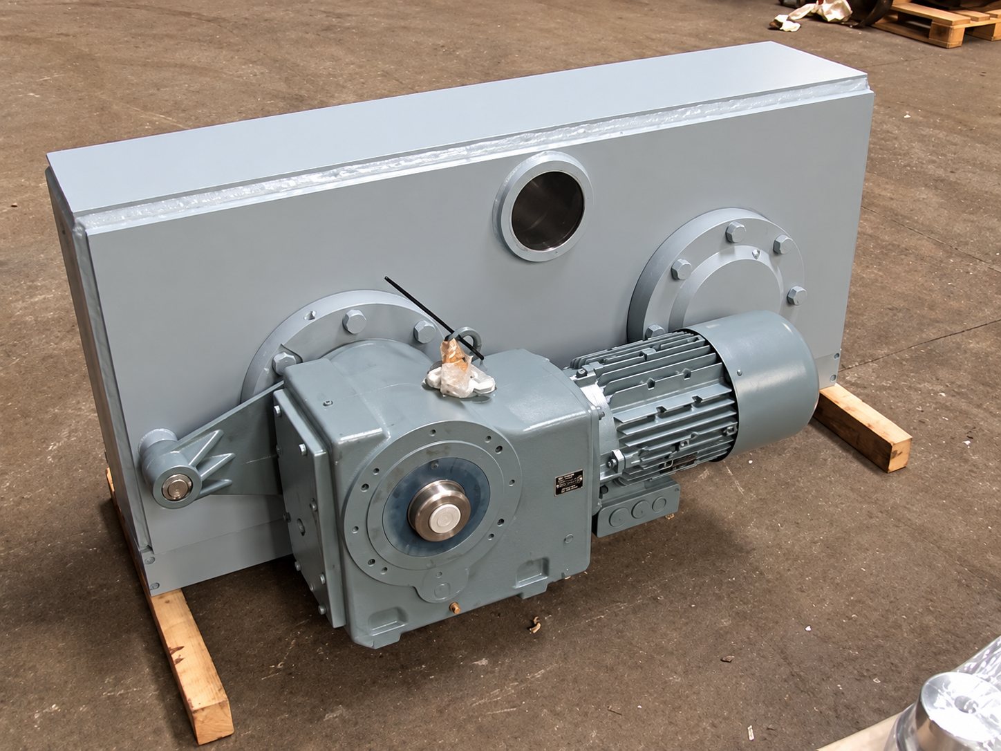 Grand réducteur industriel gris avec moteur électrique posé sur des cales en bois